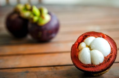 İki Olgun soyulmamış meyveler ahşap bir masa üzerinde arka plan üzerinde mangosten yarım soyulmuş.