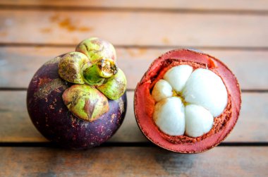 Olgun bütün mangosten ve ahşap bir masa üzerinde bir yarım kesilmiş meyve.