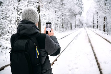 Bir adam bir sırt çantası ile telefonda karlı ormanda çalışan tramvay rayları Fotoğraf Arşivi.