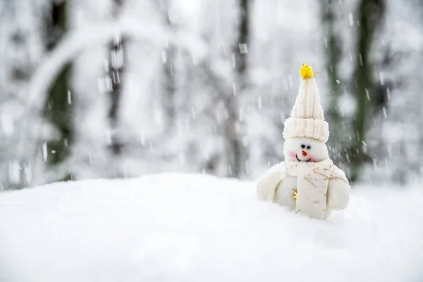 一个面带微笑的雪人戴着帽子 戴着围巾 在飘落的雪下的雪堆里 — 图库照片