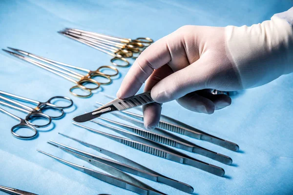The scalpel in the hands of the surgeon on the background of medical instruments in the operating room.