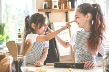 İki kız kardeş birlikte tatlı pişirirken birbirlerinin burunlarını unla sürüyorlar..