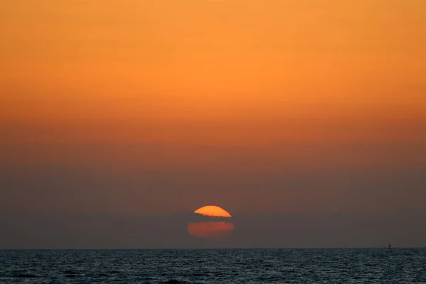 Fiery red sky lighting over the horizon at sunset. The sun sets over the horizon in the Mediterranean Sea in northern Israel