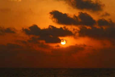Kırmızı bulutlu gökyüzünün arka planında kızıl-sıcak güneş 