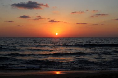 Kırmızı bulutlu gökyüzünün arka planında kızıl-sıcak güneş 