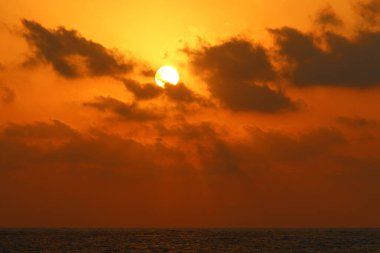 Kırmızı bulutlu gökyüzünün arka planında kızıl-sıcak güneş 