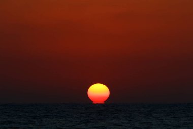 Kırmızı bulutlu gökyüzünün arka planında kızıl-sıcak güneş 