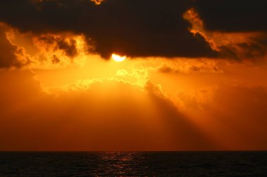 Kırmızı bulutlu gökyüzünün arka planında kızıl-sıcak güneş 