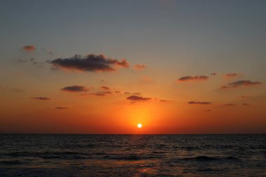 Kırmızı bulutlu gökyüzünün arka planında kızıl-sıcak güneş 