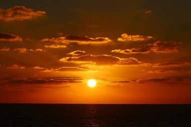 Kırmızı bulutlu gökyüzünün arka planında kızıl-sıcak güneş 