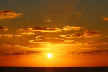 Kırmızı bulutlu gökyüzünün arka planında kızıl-sıcak güneş 