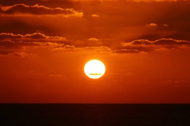 Kırmızı bulutlu gökyüzünün arka planında kızıl-sıcak güneş 