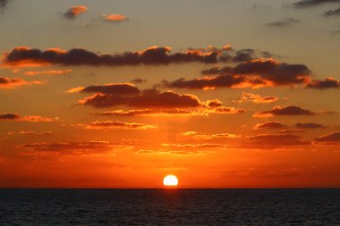 Kırmızı bulutlu gökyüzünün arka planında kızıl-sıcak güneş 