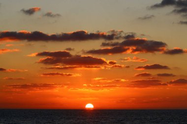 Kırmızı bulutlu gökyüzünün arka planında kızıl-sıcak güneş 