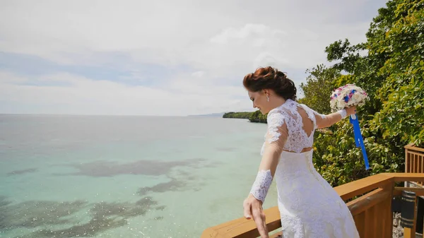 A dazzling bride enjoys happiness from the height of the balcony overlooking the ocean and reefs. Flight of love. Exotic Filipino Tropics. Shooting in motion.