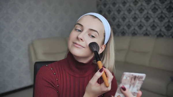 Blonde applying facial powder to herself with a brush.