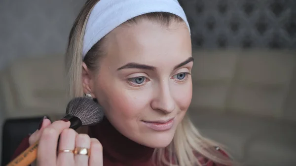 Blonde applying facial powder to herself with a brush.