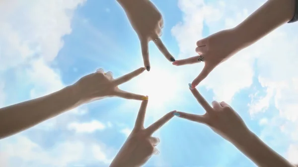 People forming star shape with their fingers against the blue sky with shining rays of the sun.