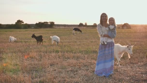 Mutter hält eine einjährige Tochter auf dem Arm auf einem Dorfplatz mit Ziegen und einer Kuh.