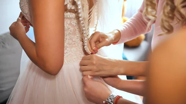 Brides girlfriend helps bride dress up her wedding dress.
