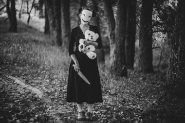 Korkunç maskeli kadın oyuncak ayıyı mutfak bıçağıyla tutuyor.