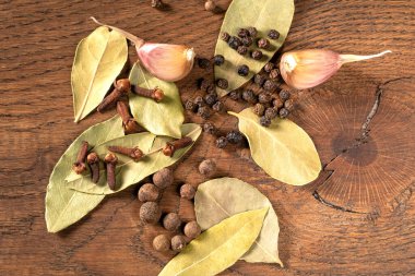 Bu resim defne yaprağı, sarımsak, biber ve karanfilleri de içeren nefis bir baharat düzenini iyi kullanılmış bir mutfak masasında ustalıkla sergiliyor, canlı renklerini ve dokularını vurguluyor..