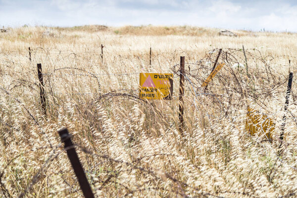 A sign reading "Danger Mines!" hangs from a barbed wire fence in the Golan Heights, near the border with Syria, Israel