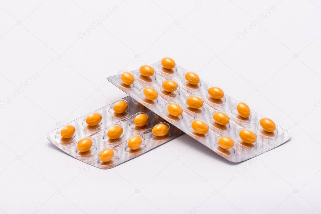 Two full sealed packages with yellow oval shaped pills lie on a white background