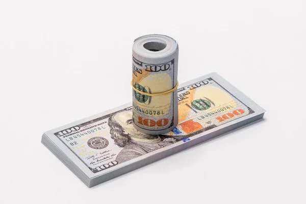 Ein Bündel amerikanischer Dollars in Stückelungen von 100-Dollar-Scheinen zusammengerollt und zusammen mit einem einfachen Gummiband mit einem Stapel amerikanischer Dollars in Stückelungen von 100-Dollar-Scheinen isoliert auf weißem Hintergrund gehalten. — Stockfoto