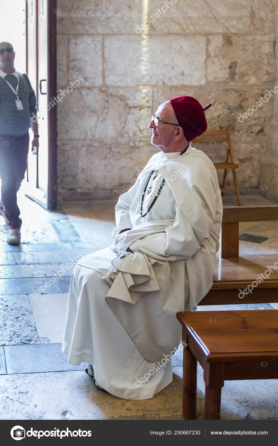 A Church Attendant In White Clothes Is Sitting On A Bench In The