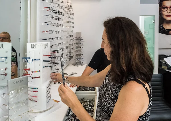 한 여성이 안경을 들고 스탠드 앞에 서서 이스라엘 나하리야 시의 검안 가게에서 독서용 안경을 선택합니다. — 스톡 사진