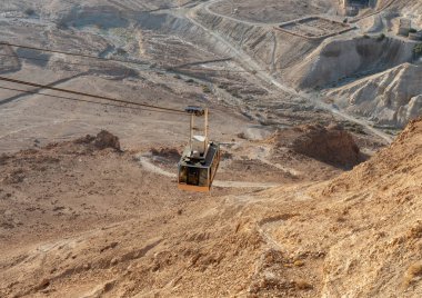 Teleferik kabini, İsrail 'deki Massada kalesinin harabeleriyle alt teleferik istasyonundan dağın tepesine doğru hareket ediyor.