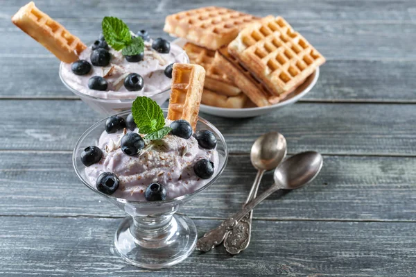 Cottage cheese dessert with blueberries in a glass cup and homemade Viennese waffles on a wooden background