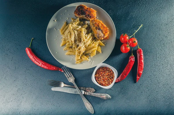 Penne pasta with pesto sauce and fried cutlets and turkey, hot chili and cherry tomatoes