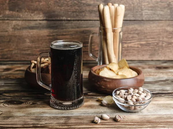 Dark beer in a mug. Snacks for beer on a wooden table. Chips, croutons, bread sticks