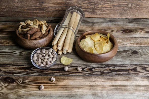 Snacks for beer on a wooden table. Chips, croutons, bread sticks and pistachios