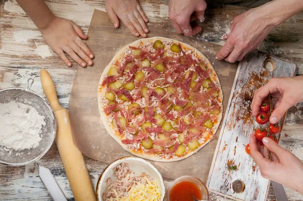 Cooking pizza with mom. Mom and her children make delicious pizza with prosciutto and cherry tomatoes. Food concept. Top view
