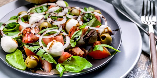 Food banner delicious salad made from fresh herbs with mozzarella, tomatoes, olives, onions and balsamic dressing. Italian traditional cuisine. Fork and knife