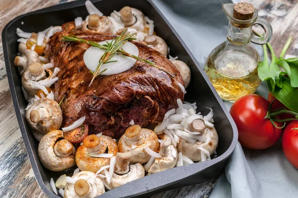 Marinated lamb with mushrooms, spices and herbs in a cast-iron mold on a wooden background. Tomatoes and olive oil. Halal meat and food