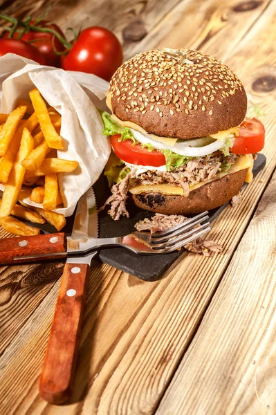 Close-up big homemade hamburgers, french fries and dark beer. Hamburgers with beef, tomatoes, cheese, meat and salad on a wooden table.