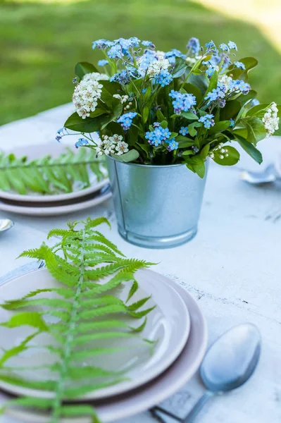 Close-up forget-me-not flowers and fern leaves. Outdoor white table decoration in rustic style. Vertical shot
