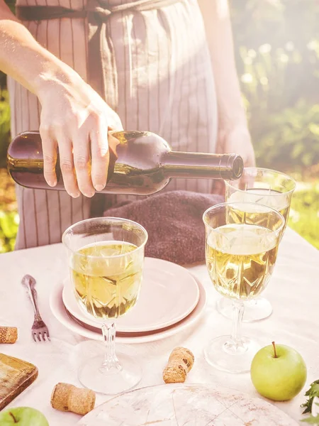 Woman pouring white wine. Dinner concept with wine in the fresh air. Fish and salads with vegetables and herbs. Mediterranean Kitchen. Vertical shot