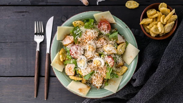 Food banner. Caesar salad with quail egg, fried chicken, parmesan cheese and croutons on a dark rustic background. Horizontal shot