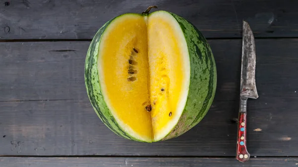 Food banner. Yellow watermelon and knife on a dark wooden background. Top view
