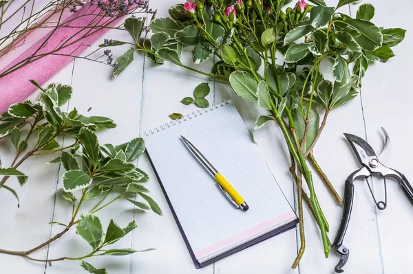 Florist workplace: flowers, accessories, tools and a notebook for records. Top view