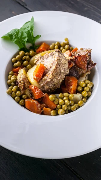 Vertical food banner Baked meat with vegetables. Potatoes, carrots, green peas and turkey meat on a white plate