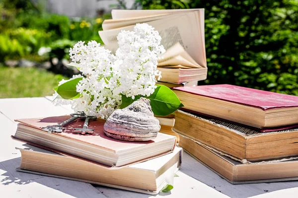 Old books and a branch of white lilac on a wooden table. Vintage composition
