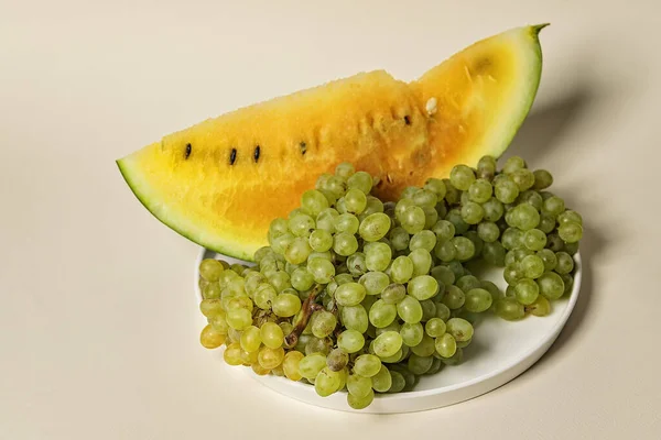 Fresh juicy slice of yellow watermelon and sweet quiche-mish grapes on a beige background. Organic vegetables and fruits