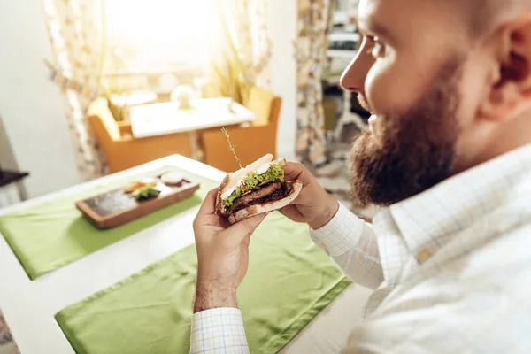 Voltar vista homem morder sanduíche comer no café — Fotografia de Stock