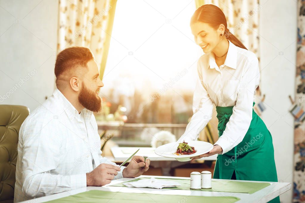 Girl waiter serves his dish in restaurant to a man